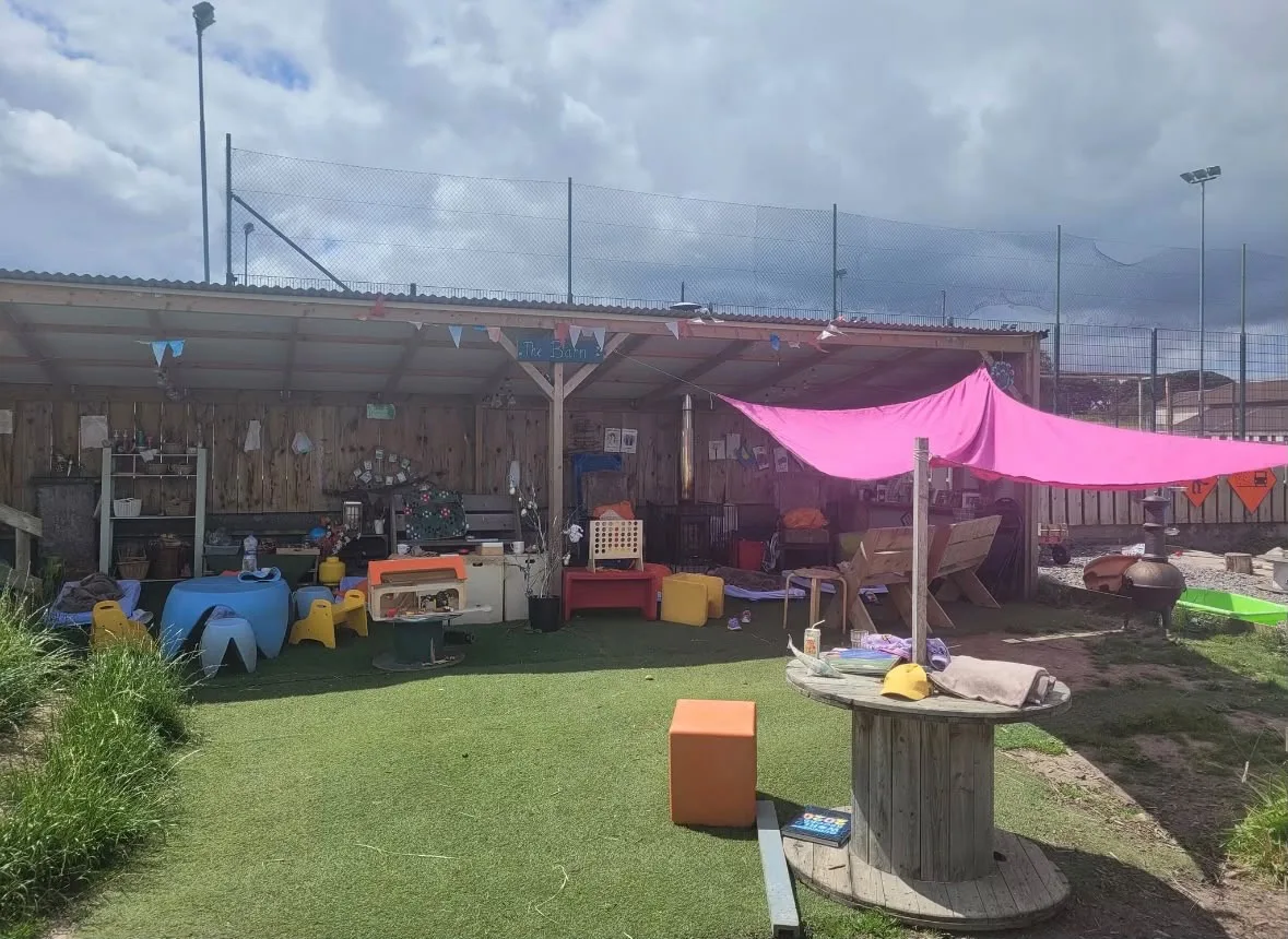 Outdoor tables and play materials beneath colourful shade sails