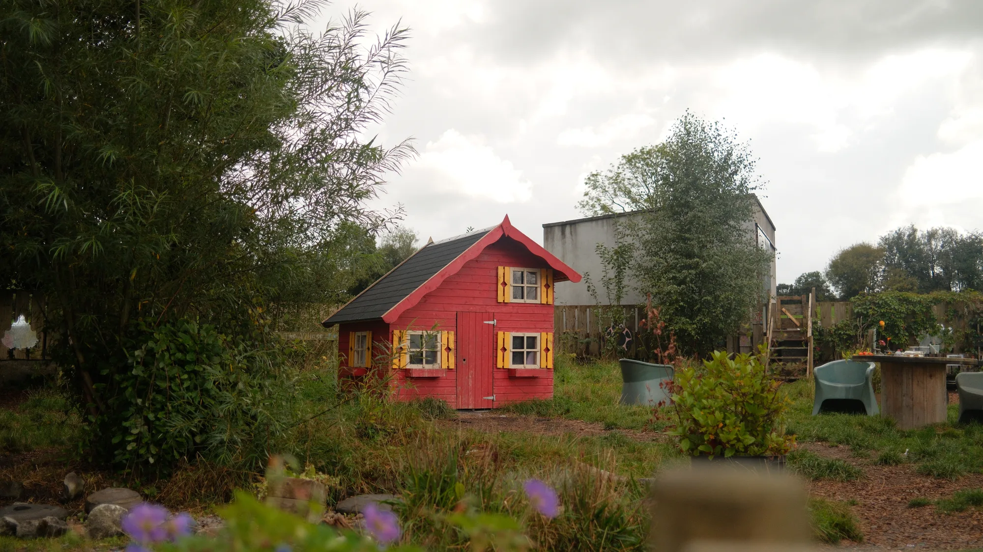 The red playhouse across the planted garden