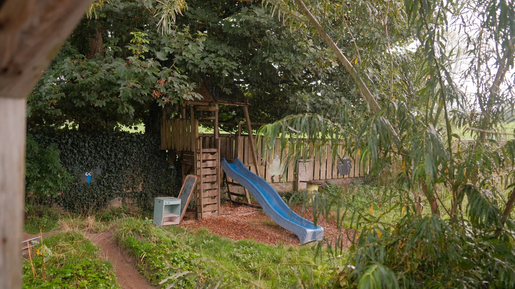 The blue slide beneath a large tree in the play garden